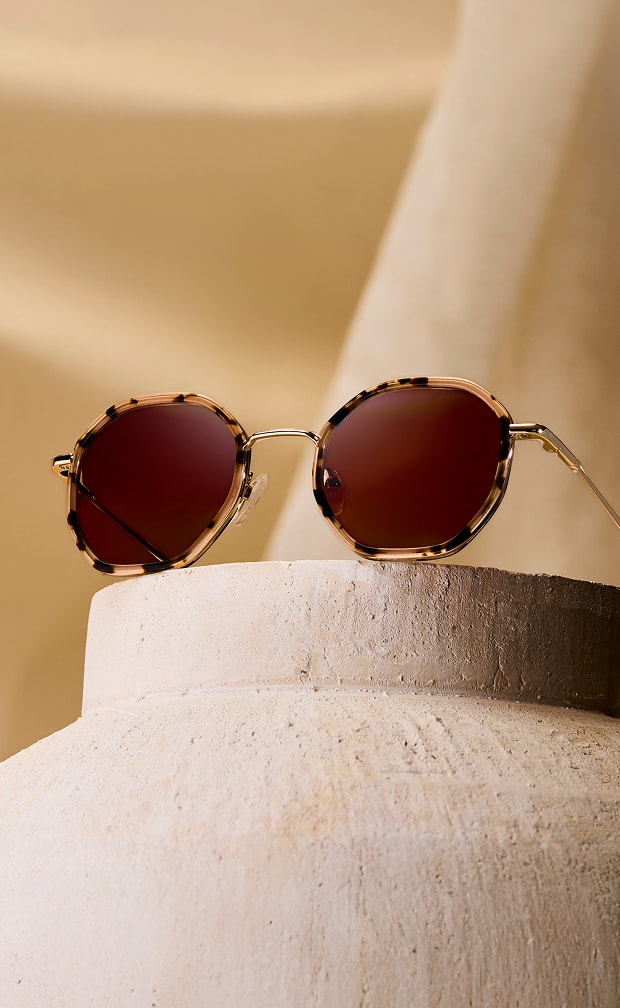 Geometric tortoiseshell Zenni glasses with brown lenses, on a beige stone background.