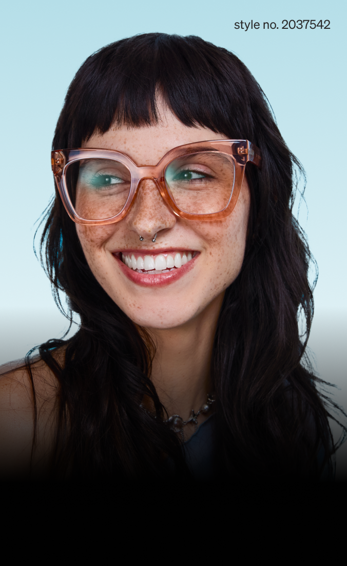 A smiling person with long dark hair and freckles wears oversized clear-framed glasses and a septum piercing. The background is a soft gradient of light blue. Style no. 2037542.