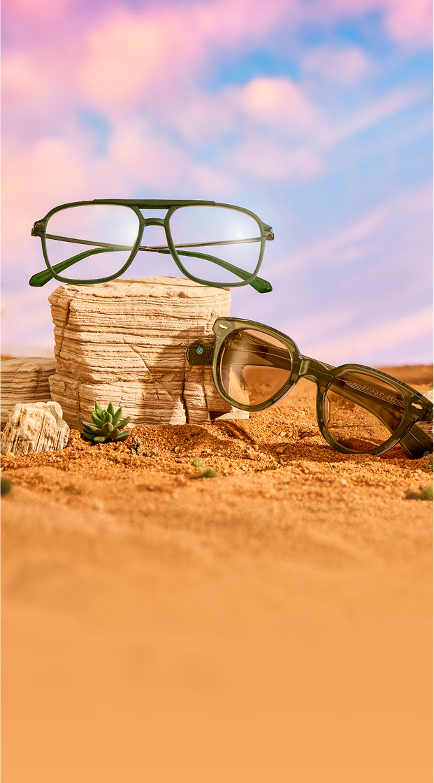 Three pairs of stylish sunglasses are displayed on layered rock formations in a desert-like setting, with a dramatic pink and blue sky in the background.