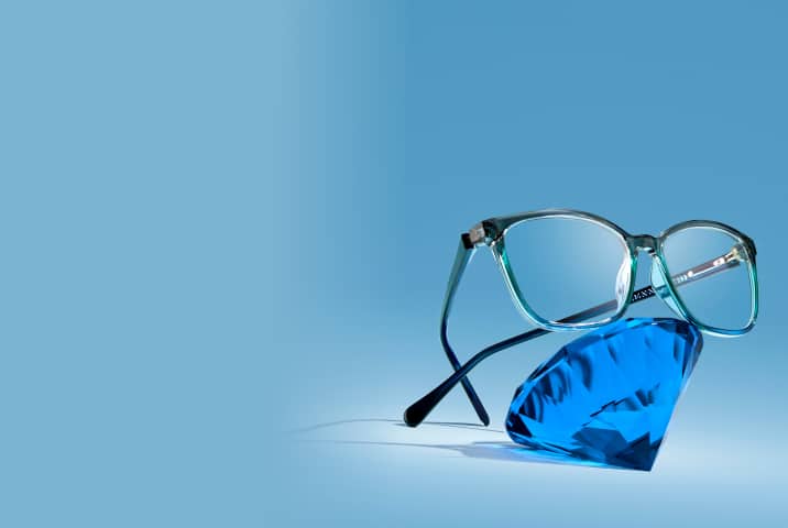 Three-tone gray, blue, and turquoise glasses resting on a giant sapphire gem, on a blue background.