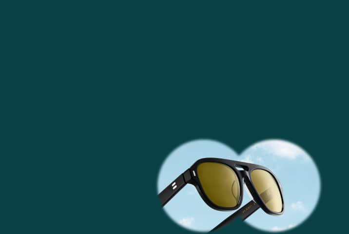 Black aviator sunglasses with yellow-tinted lenses framed within a binocular-shaped view showing a blue sky with light clouds, set against a dark forest green background.