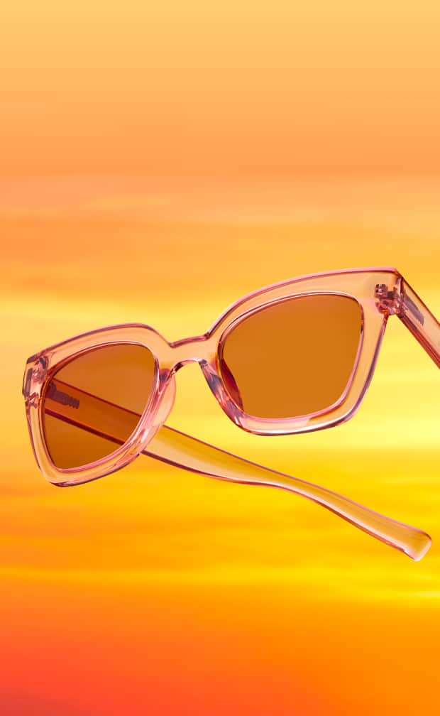 Lunettes de soleil papillon pêche translucides flottant sur un fond de coucher de soleil incandescent orange et jaune.