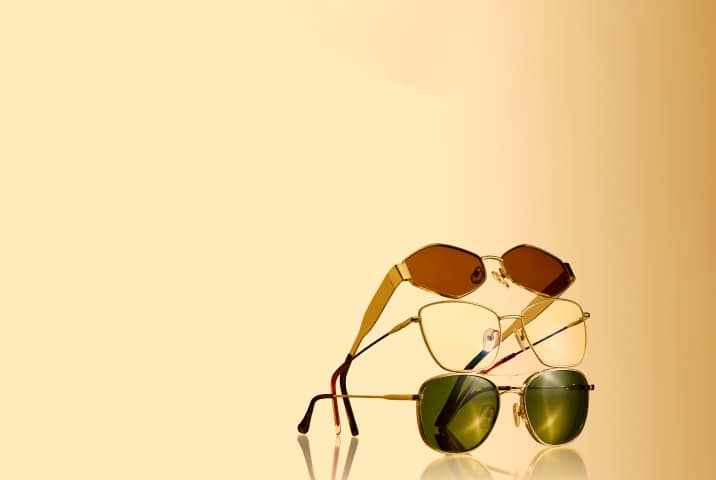 Stack of four stylish gold-frame sunglasses with tinted lenses, arranged vertically on a golden gradient background.