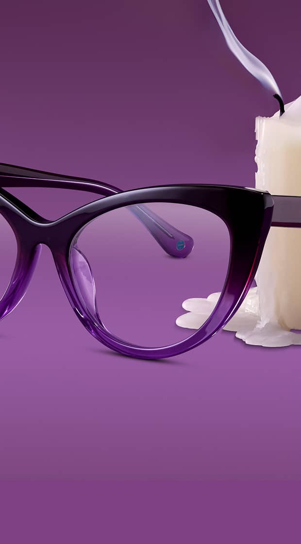 Close-up of dark purple gradient cat-eye eyeglasses resting next to a smoking white pillar candle against a purple background.
