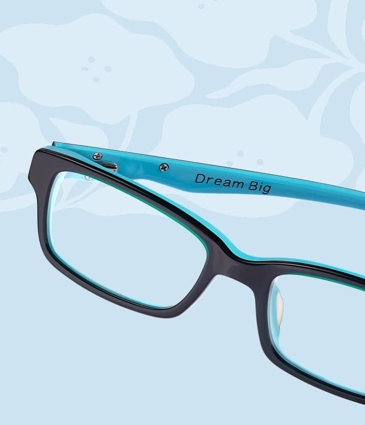 Gros plan sur des lunettes rectangulaires noires avec une couche intérieure bleu cyan vif gravée « Dream Big » sur la branche, sur fond floral bleu clair.