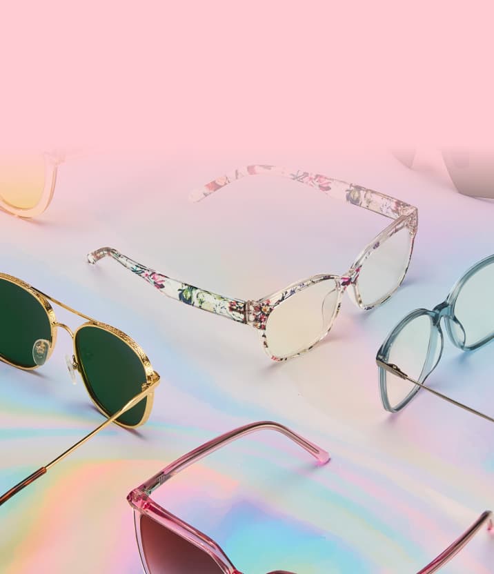 Array of colorful sunglasses and eyeglasses in various frame styles arranged on a pastel rainbow background fading to soft pink.