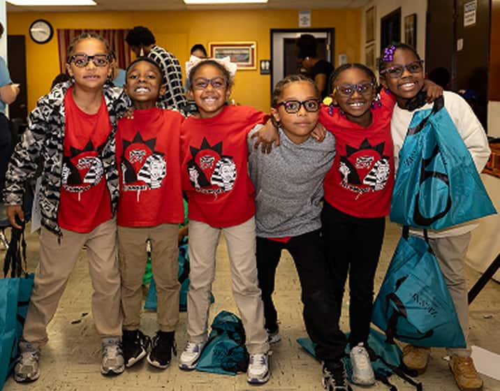 Six smiling children with Zenni giftbags posing at a Zenni Vision Screening event.
