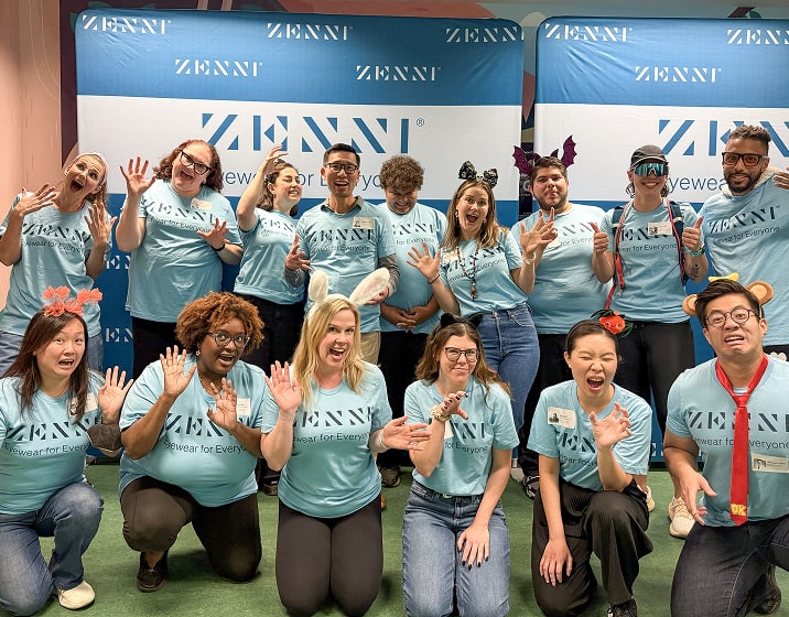 Two rows of Zenni employees wearing light teal Zenni t-shirts, posing in front of a Zenni banner.