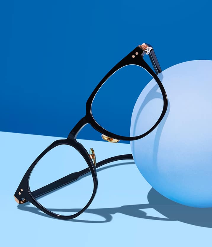 A product photo of Zenni black round glasses on a medium and light blue background, casting a shadow.
