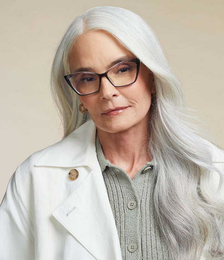 A woman with long white hair wearing Zenni Cat-Eye Reading Glasses with tortoiseshell frames, a gray ribbed sweater, and a white jacket.