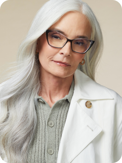 A woman with long white hair wearing Zenni Cat-Eye Reading Glasses with tortoiseshell frames, a gray ribbed sweater, and a white jacket.