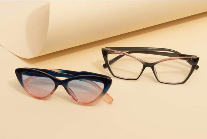 Two pairs of stylish eyeglasses on a beige background. One pair features cat-eye frames in a gradient of blue and pink, while the other pair has black frames with a subtle pink accent.