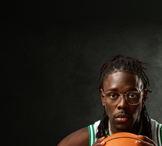 Jrue Holiday wearing Zenni glasses in a green and white jersey, holding a basketball in front of him.