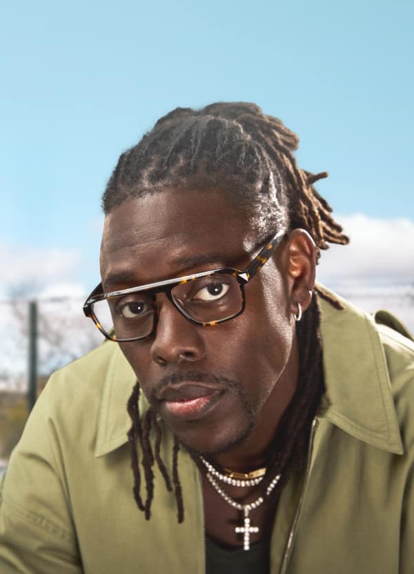 Jrue Holiday wears “Dynamo” optical glasses from his Zenni collection, paired with a green jacket, jewelry, and hair pulled back. 