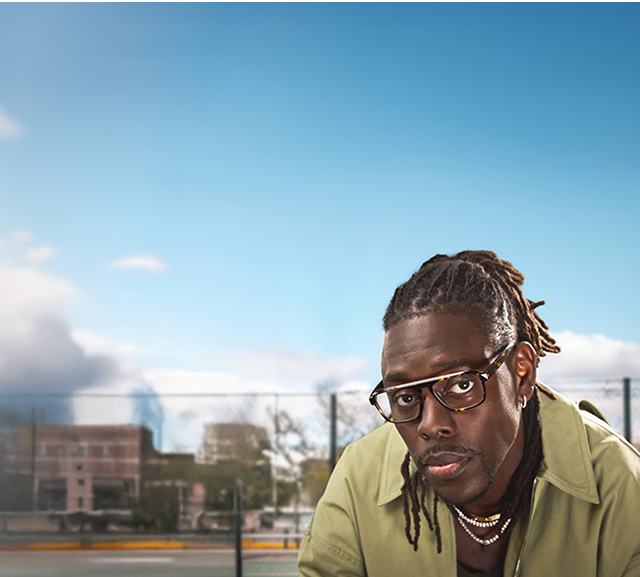 Jrue Holiday wears “Dynamo” optical glasses from his Zenni collection, paired with a green jacket, jewelry, and hair pulled back.