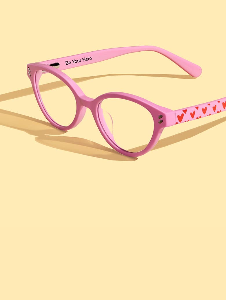 Wide angled photo of pink Zenni glasses with love heart patterned arms, on a pastel yellow background.