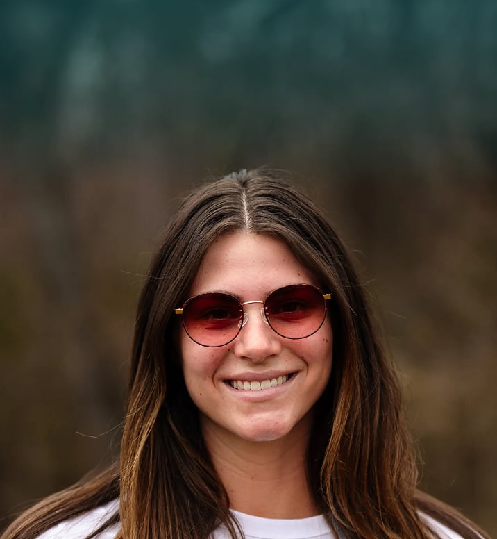 Smiling woman wearing Zenni round red-tinted lens sunglasses outdoors.