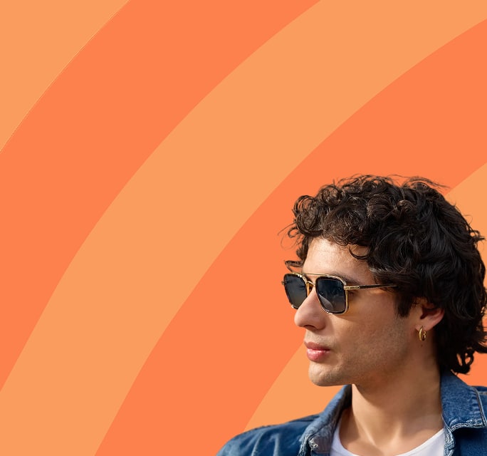 A young man with curly hair wears aviator sunglasses in profile against an orange diagonal-striped background, promoting sunglasses. 