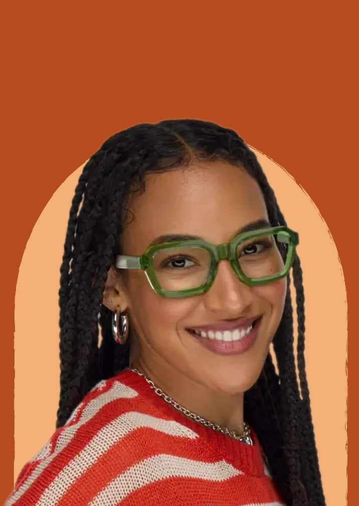 Smiling woman with long braids wearing thick green square eyeglasses against a warm terracotta and beige background.