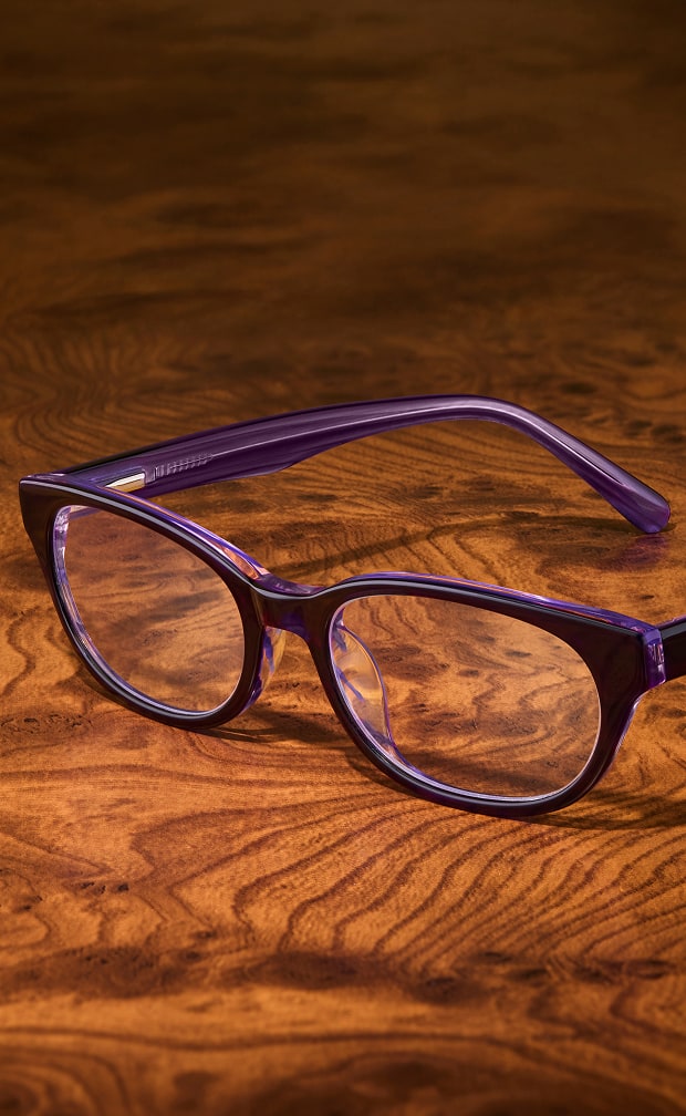 Dark purple translucent cat-eye eyeglasses resting on a warm polished wood grain surface.