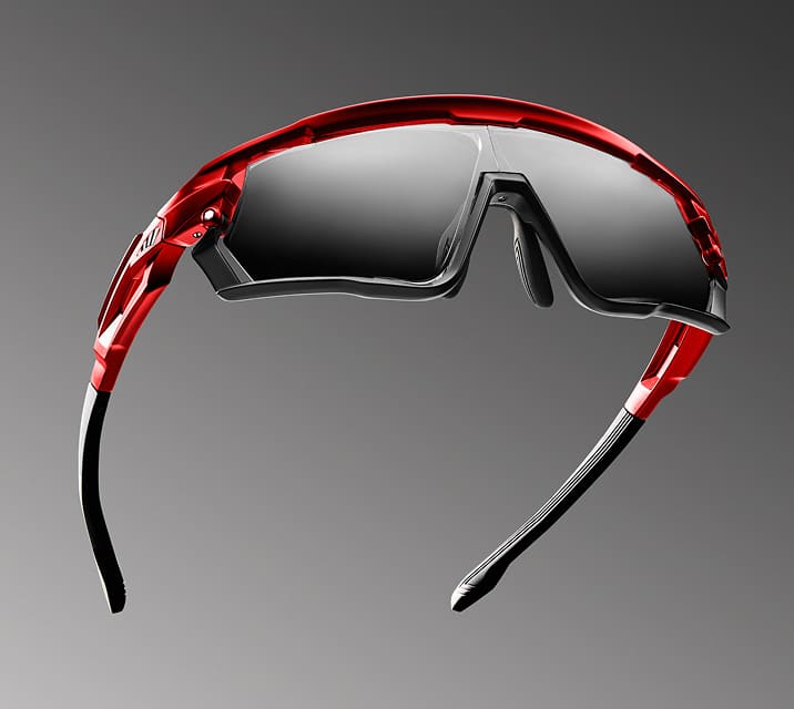 Closeup of red and black sports sunglasses with a reflective lens on a gray background.