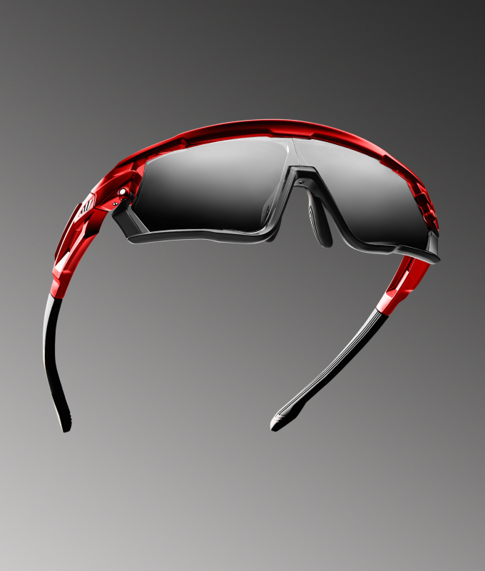 Closeup of red and black sports sunglasses with a reflective lens on a gray background.
