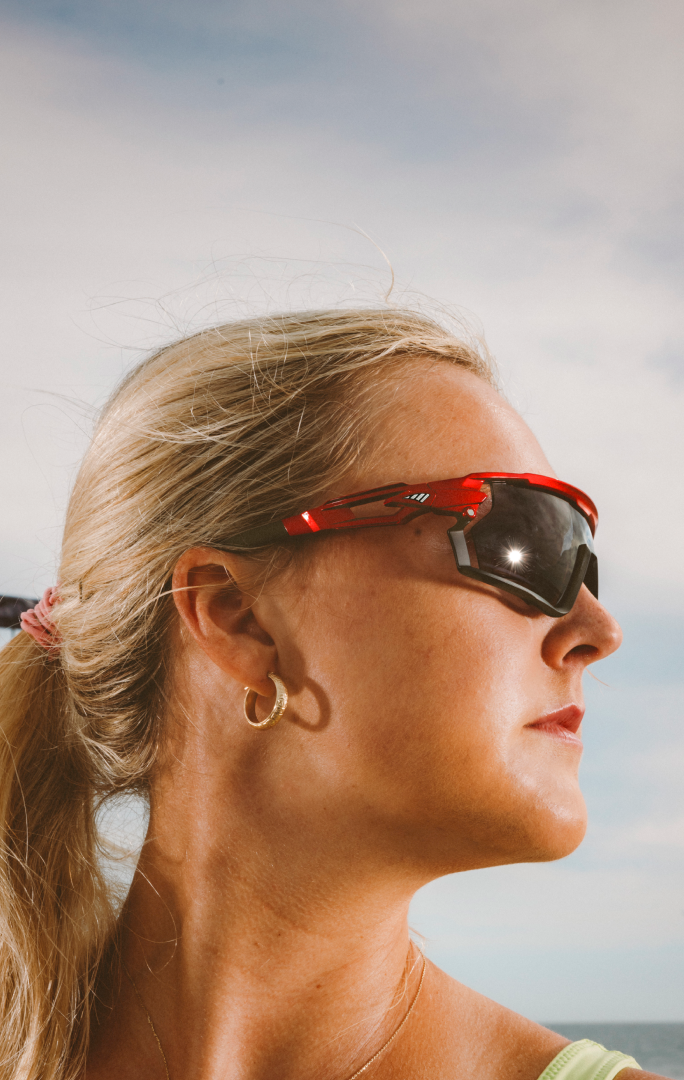 Taryn Kloth wearing red sunglasses with the quote, 'The adjustable nose helps my frames stay in place, always.' Background shows an outdoor setting. 'Shop now' button below the quote.