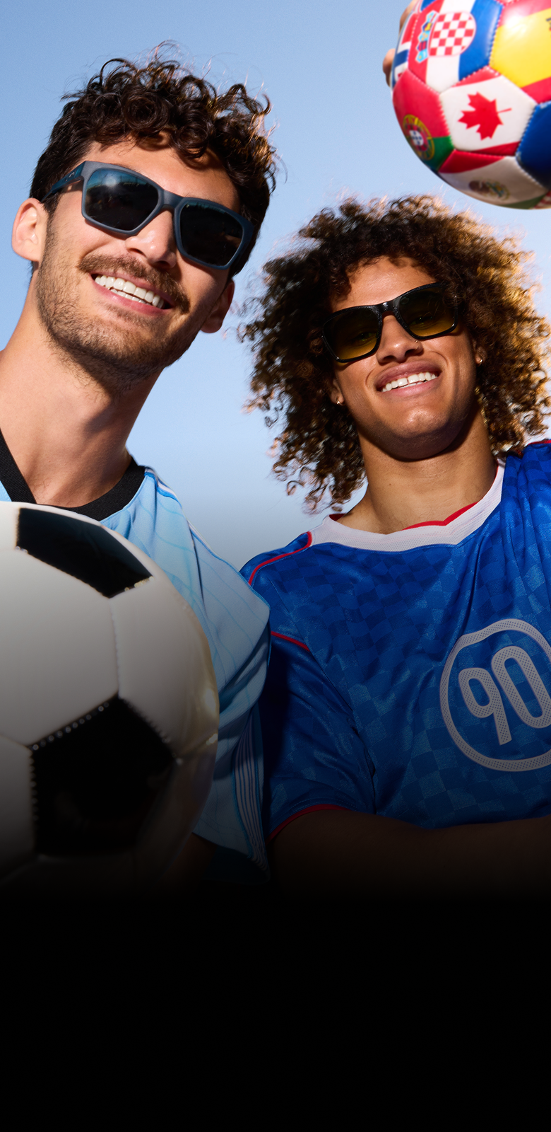 Two soccer fans wearing Zenni sunglasses, smiling with soccer balls against a blue sky.