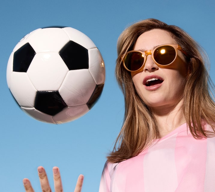 Woman wearing Zenni sunglasses with a soccer ball against a blue sky.
