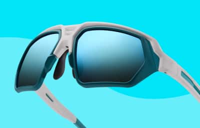 Close-up of white and teal Zunnies sunglasses with wide blue mirrored lenses on a light blue background.