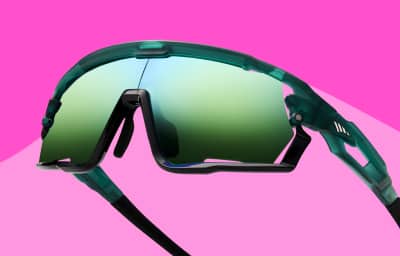 Close-up of green Zunnies sunglasses with green mirrored lenses and angular frame, set on pink background.