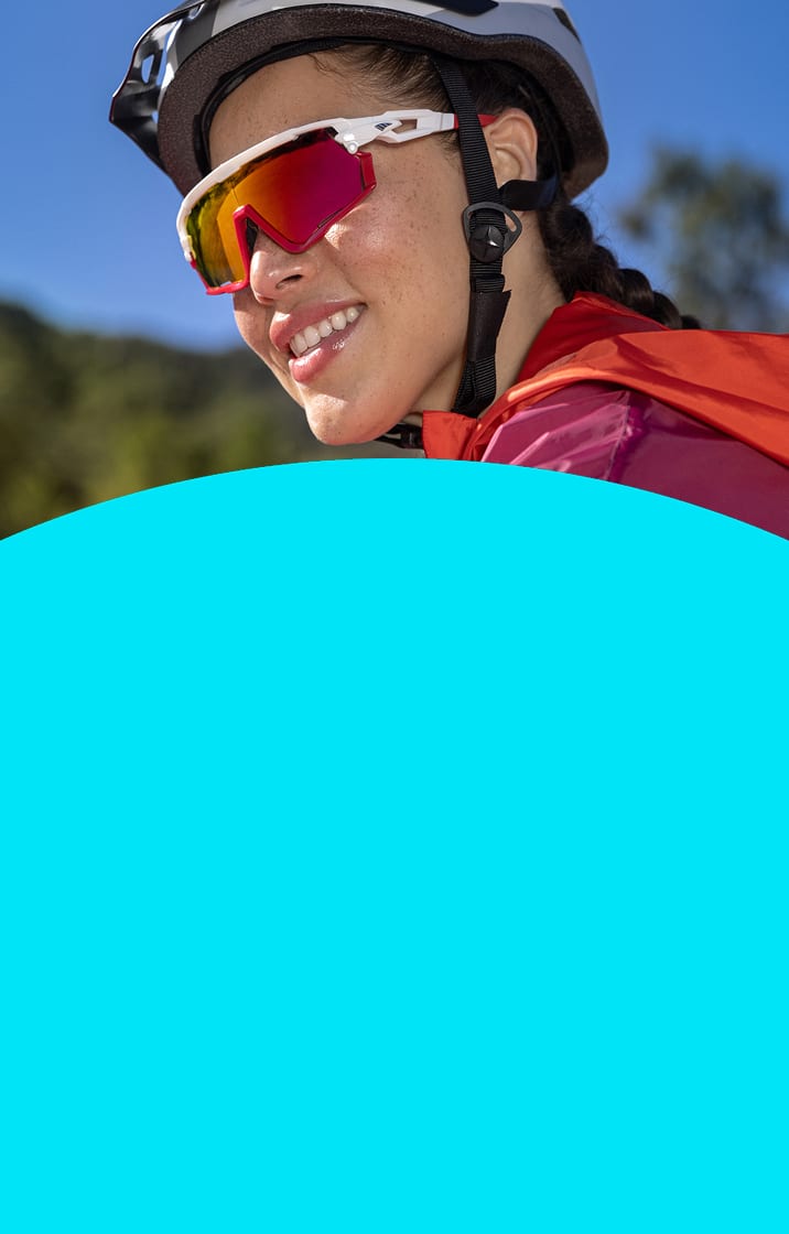 Woman outside wearing a cycling helmet and Zunnies cycling sunglasses with red mirrored lenses.