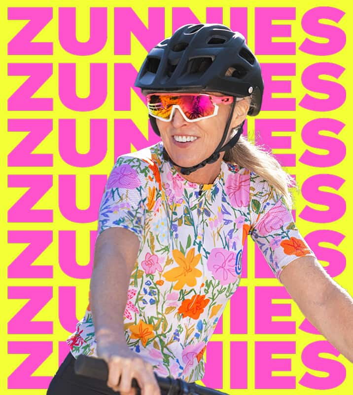 Woman wearing Zunnies sports sunglasses with reflective lenses and a cycling helmet and on a pink and yellow Zunnies background.