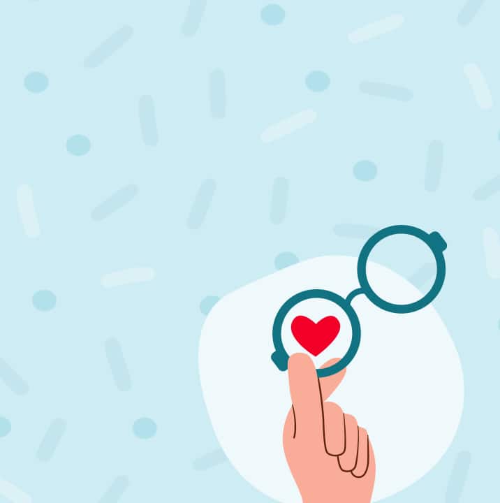 An illustration on a light blue background with faint sprinkles and dots. A hand is making a finger heart gesture inside the lens of a pair of round, dark-rimmed glasses, with a red heart visible inside the lens.