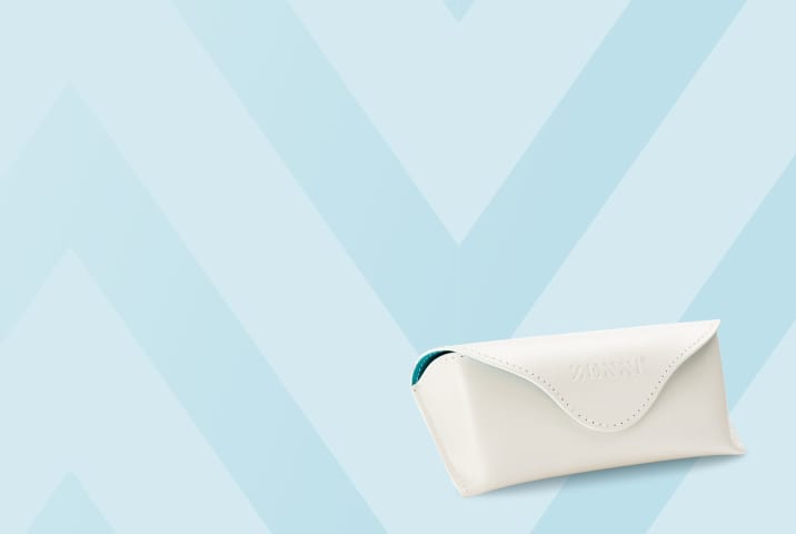A white faux-leather triangular eyewear case with an embossed Zenni logo and teal interior lining, shown against a light blue chevron background.