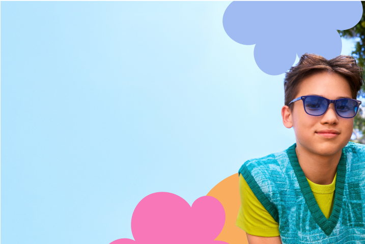 The image shows a preteen with short brown hair wearing blue sunglasses and a teal-and-white patterned knit vest over a bright green shirt. The background features overlapping abstract shapes in soft hues of blue, purple, orange, and pink, with part of the scene showing blurred greenery, suggesting an outdoor setting with trees.
