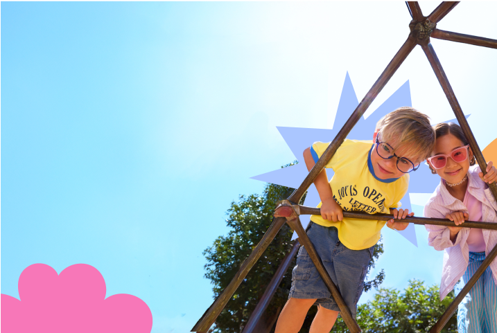 Three children wearing glasses lean on a metal play structure with a colorful backdrop.