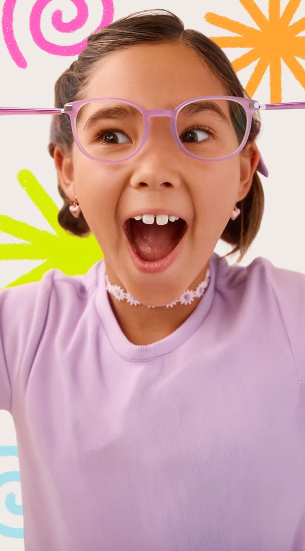 Close-up of an excited young girl with an open-mouthed expression, playfully pulling back the flexible temple arm of her purple round eyeglasses, set against a white background decorated with colorful crayon doodles.