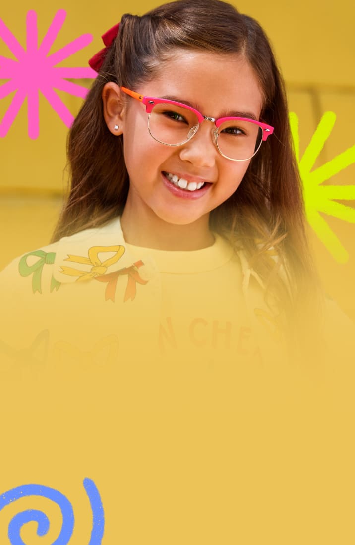 Close-up of a smiling young girl wearing bright pink and orange browline-style eyeglasses, set against a yellow brick wall background embellished with colorful hand-drawn doodle spirals and stars.