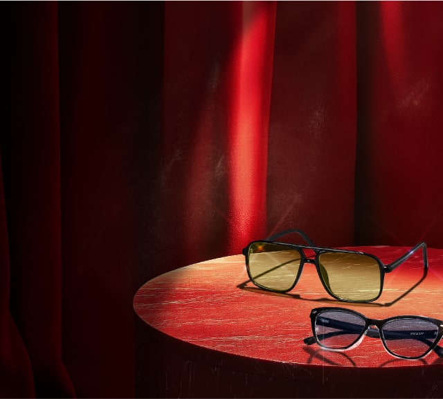 A sleek, modern pair of glasses sits on an elevated display, with cool lighting highlighting their elegant design.