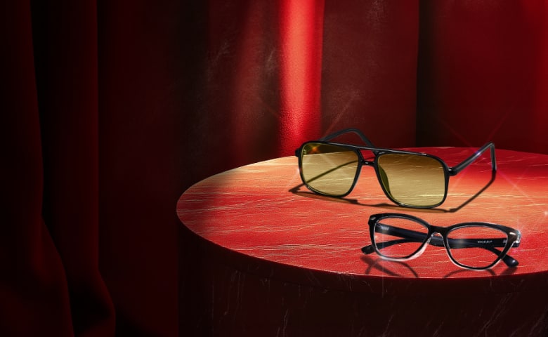 Two pairs of sophisticated glasses are displayed on a round wooden table, framed by luxurious red curtains.