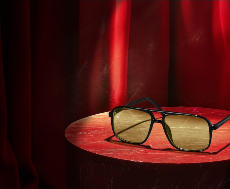 A pair of aviator glasses displayed on a round wooden table, framed by luxurious red curtains.