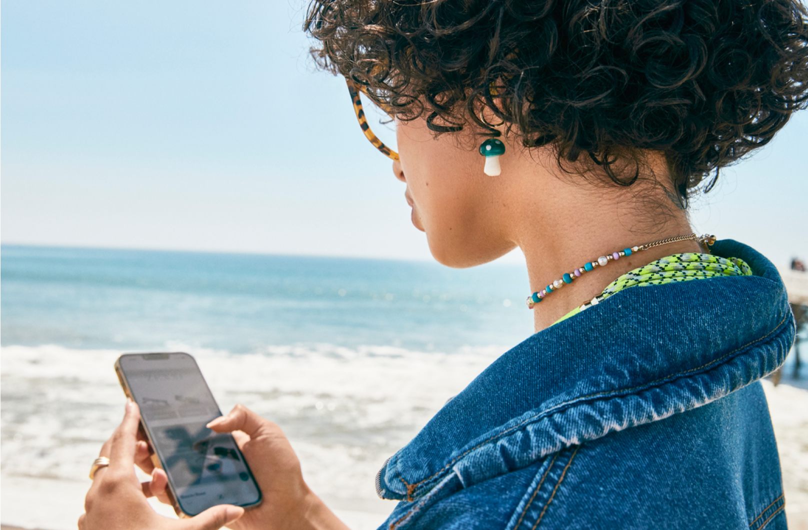 A woman is using her Blokz blue light glasses to look at her phone while on the beach.