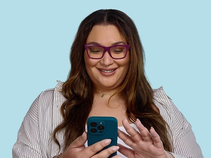 A smiling woman with long brown hair and purple glasses looks at her phone while tapping the screen.