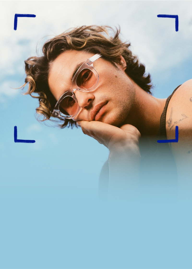 Chase Stokes wears Zenni frames with EyeQLenz featuring Zenni ID Guard lenses, posing outdoors under a bright sky.