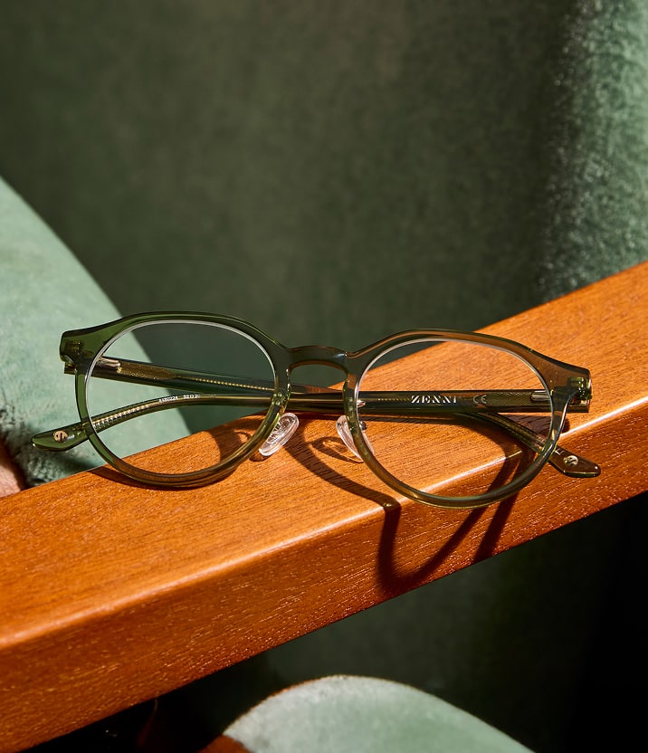 Olive green round Zenni eyeglass frames with resting on a wooden armrest.