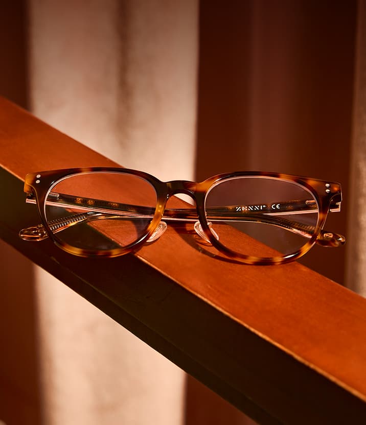 Round tortoiseshell Zenni eyeglass frames resting on a wooden armrest