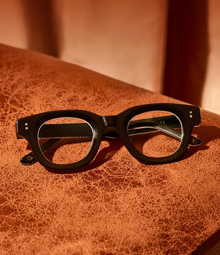 Thick black Zenni eyeglass frames displayed on a leather surface.