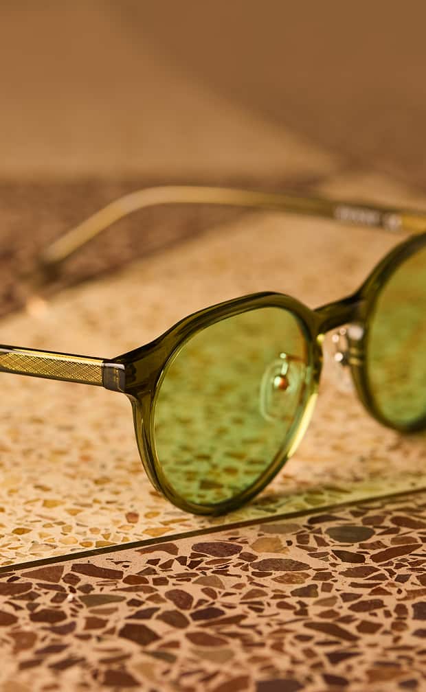 Round Zenni glasses with green lenses and gold temples on a patterned background.