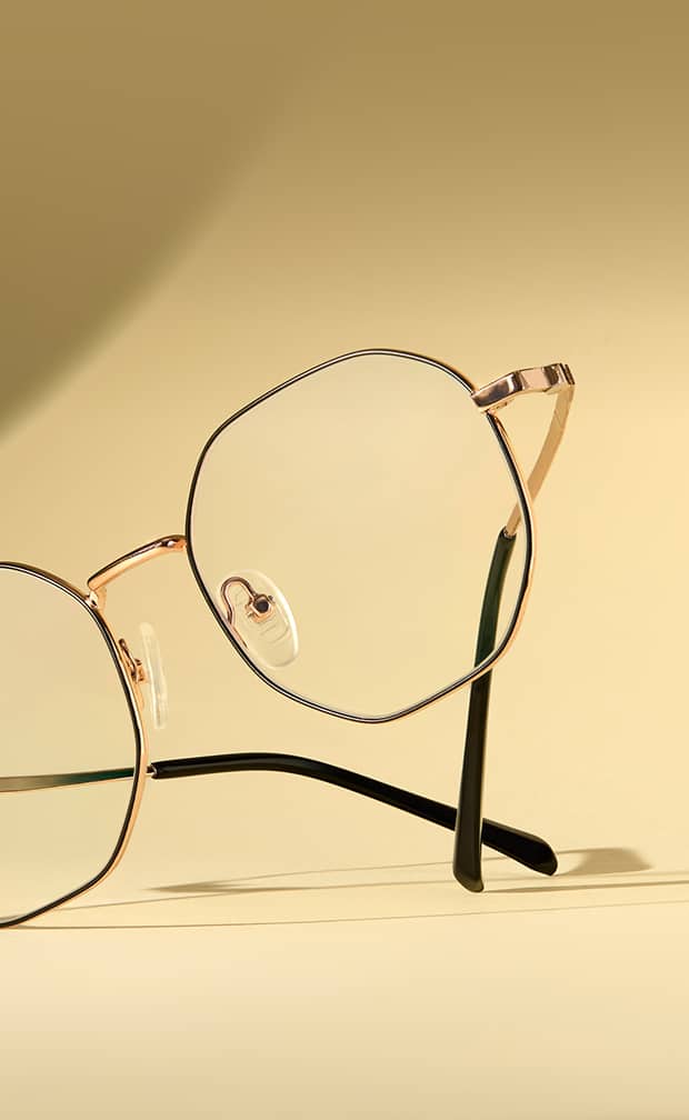 Geometric gold wireframe eyeglasses with black temple tips resting on a warm beige background.